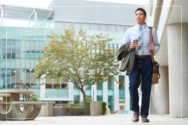 Man in business casual clothes walking outside a campus building